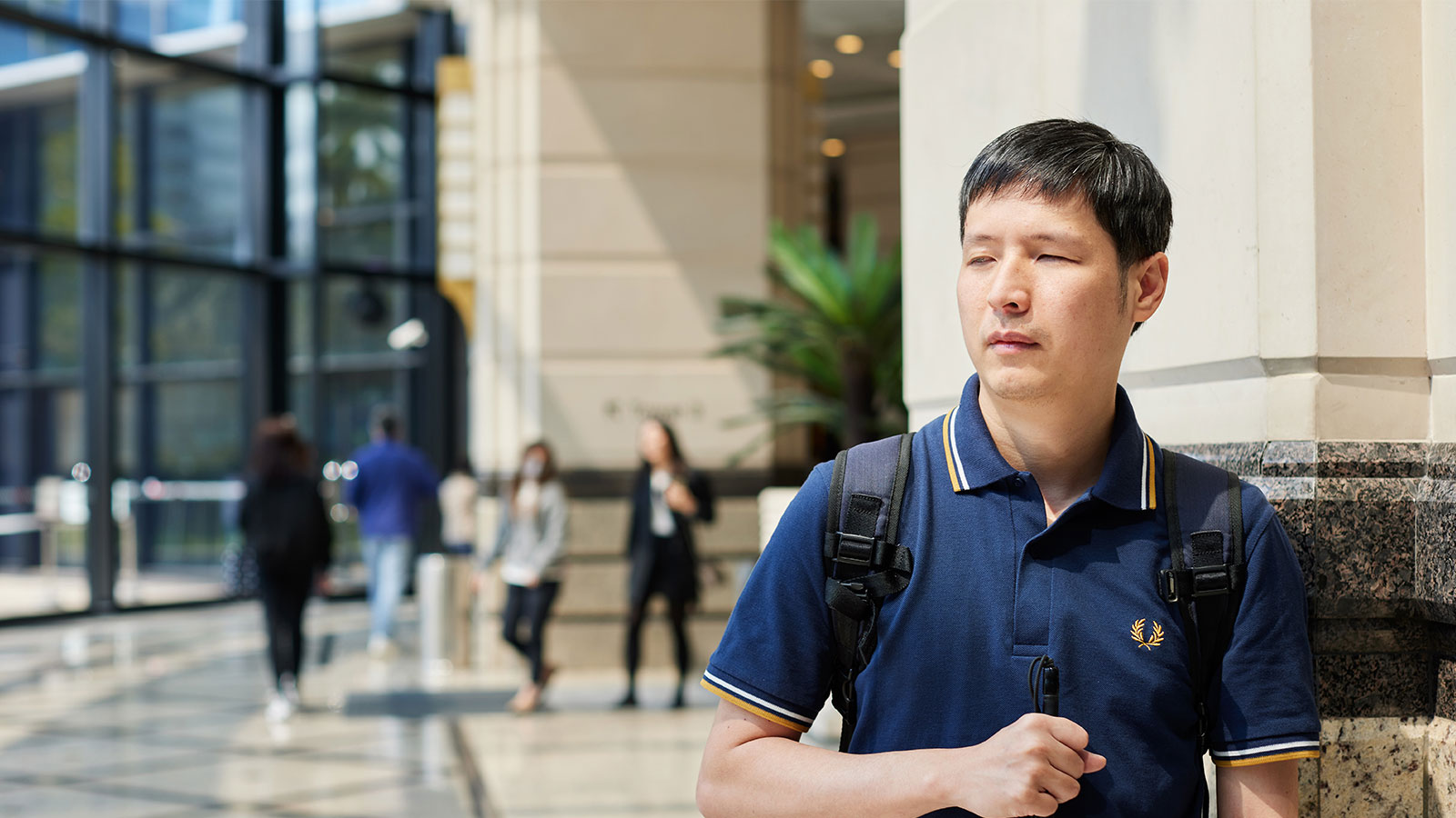 The photo shows Keny in casual clothing, holding a cane and walking through the lobby of his office in Hong Kong