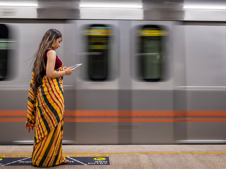 A young woman looks at a tablet while waiting for a train at a subway station, in India.