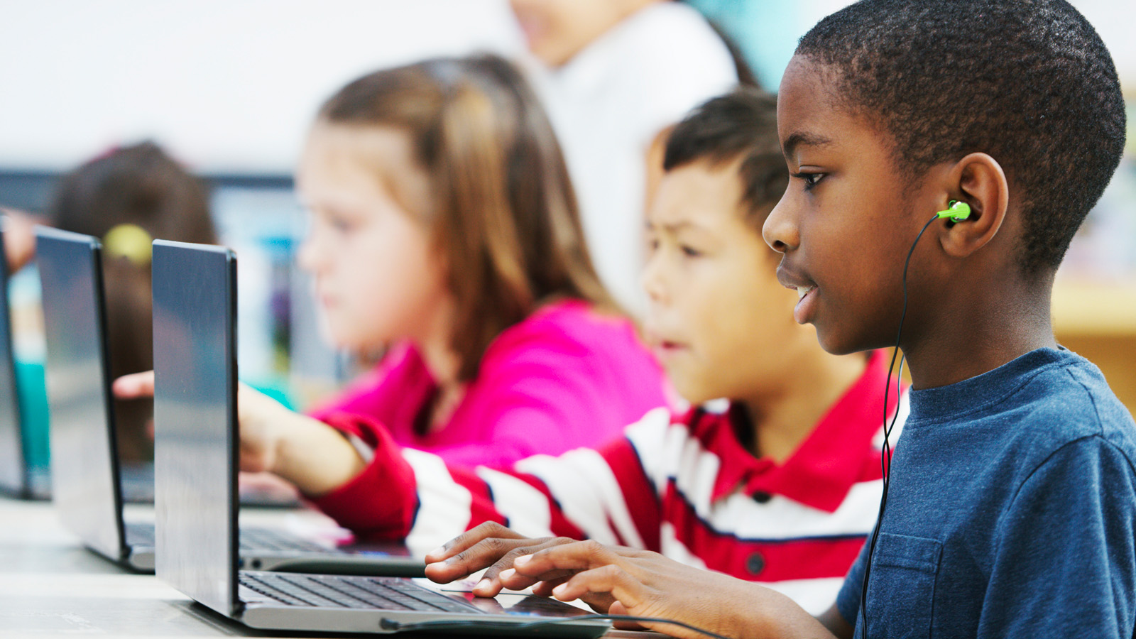 Three young children using laptops in a classroom
