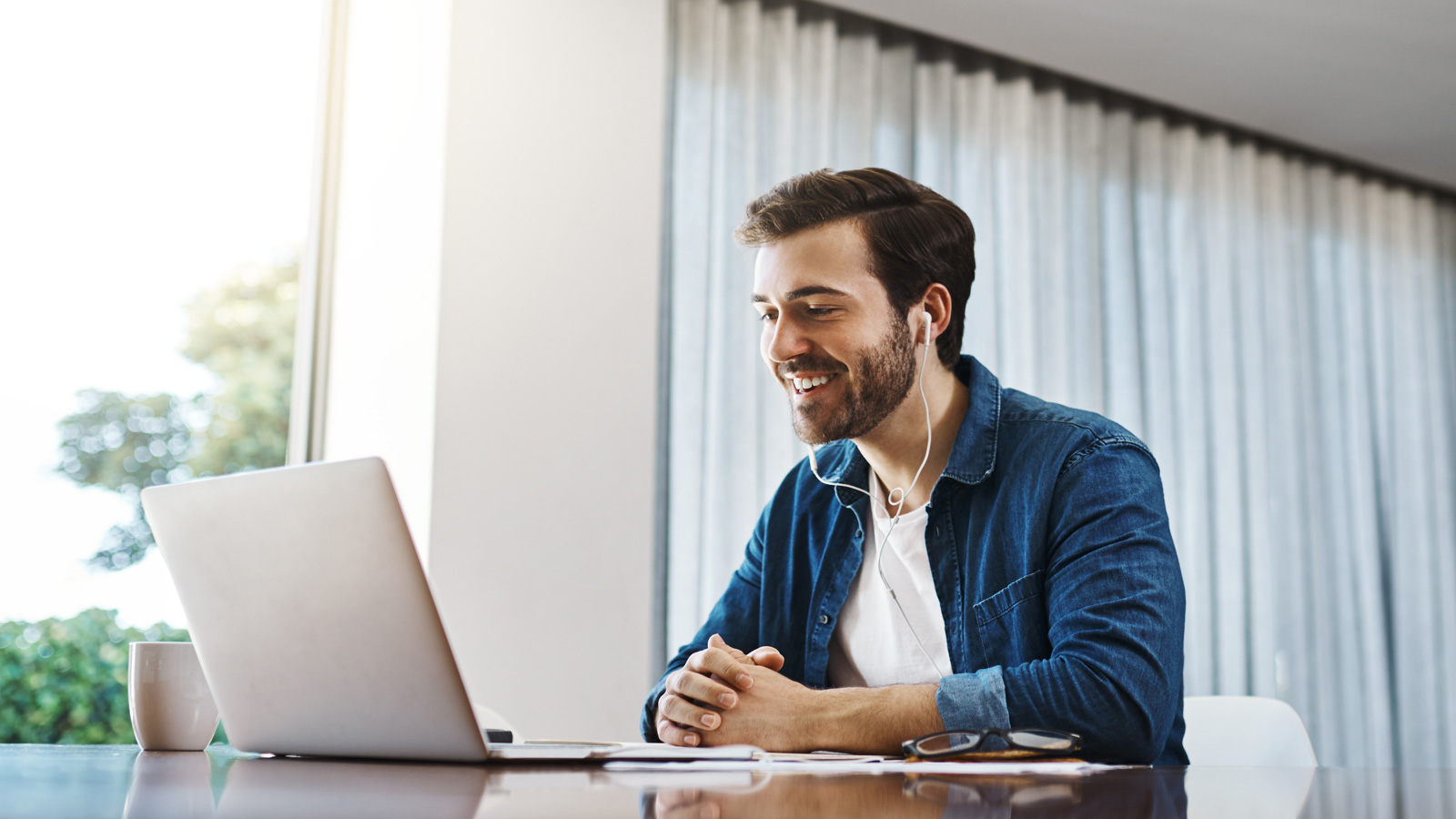 A man is taking part in a teleconference while sitting at a table in his home