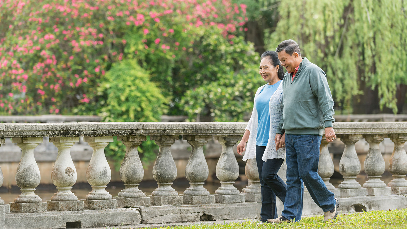 An elderly Asian couple hold hands as they walk through a park