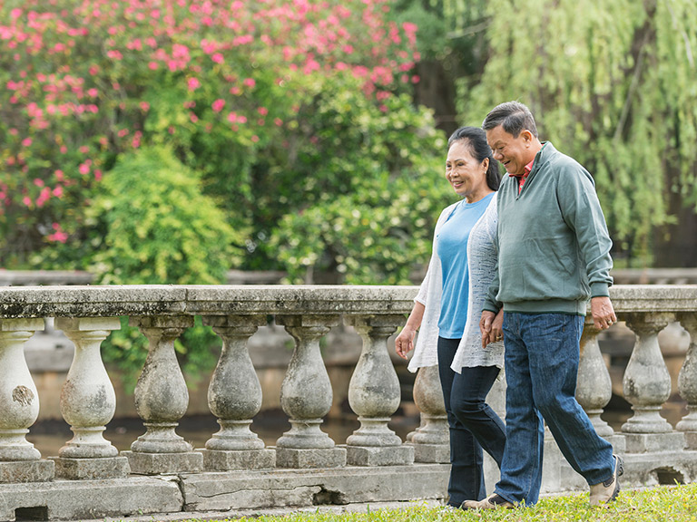 An elderly Asian couple hold hands as they walk through a park