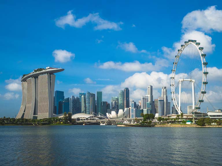 A photograph of the central business district in Singapore – the buildings are reflected in the river and the sky is blue.